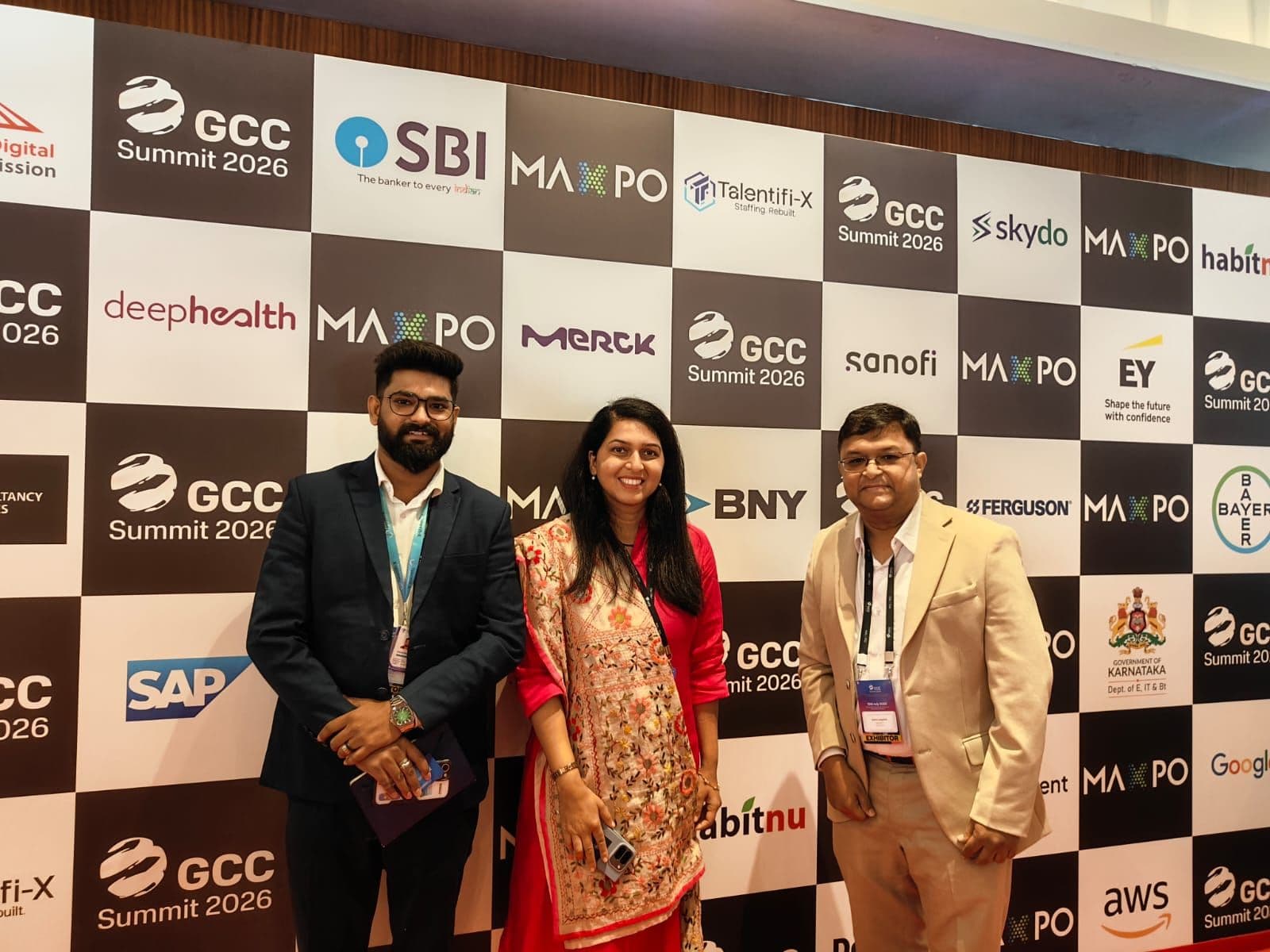 TalentiFi-X team members in front of the GCC Summit 2026 partner wall, which carries the TalentiFi-X logo alongside other sponsors.