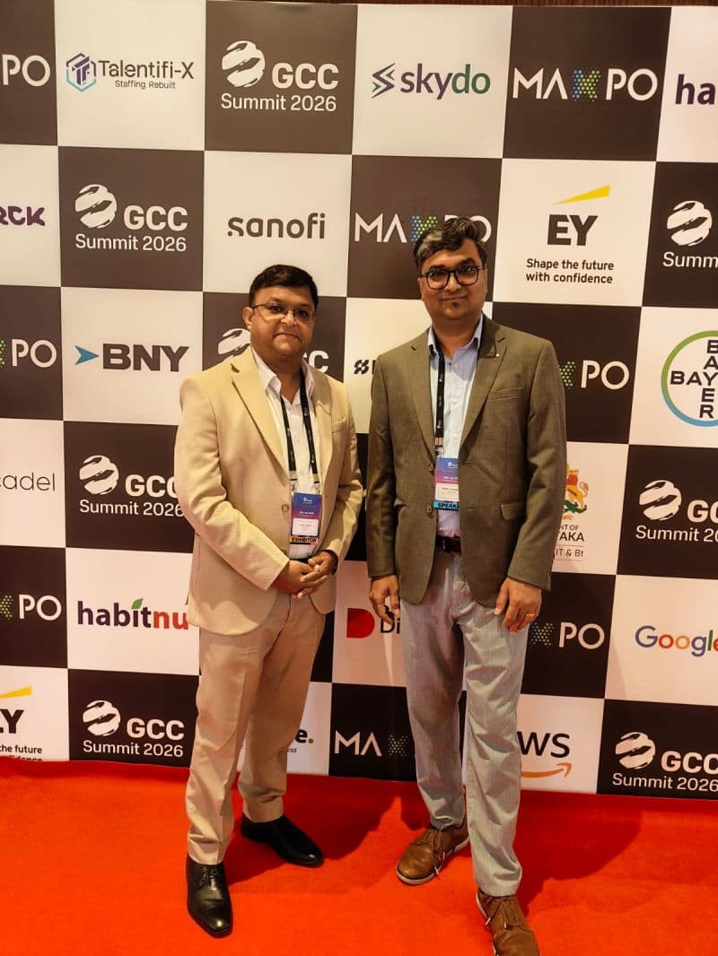 Two delegates in business attire in front of the GCC Summit 2026 sponsor wall.